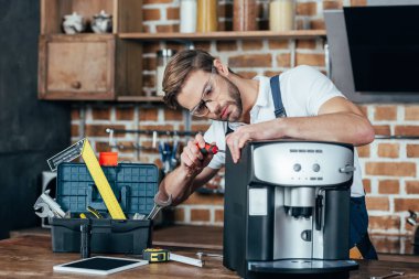 professional young repairman in eyeglasses fixing coffee machine  clipart