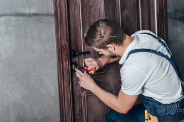 young repairman fixing door lock with screwdriver clipart