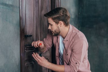 young man repairing door lock with screwdriver and flashlight clipart