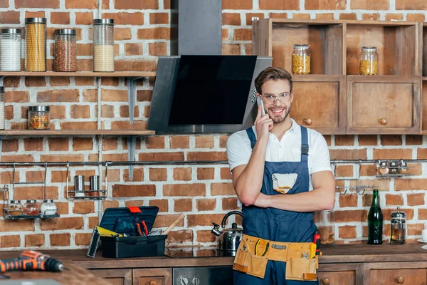 Stilig Unga Reparatör Talar Smartphone Och Ler Mot Kameran Köket — Gratis stockfoto