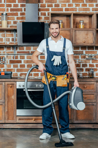 handsome young handyman holding vacuum cleaner and smiling at camera