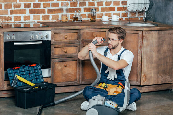 young repairman in protective glasses checking broken vacuum cleaner 