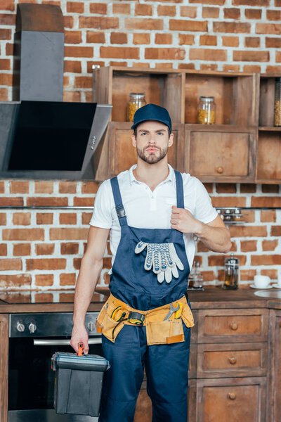 young repairman with toolbox showing thumb up and looking at camera
