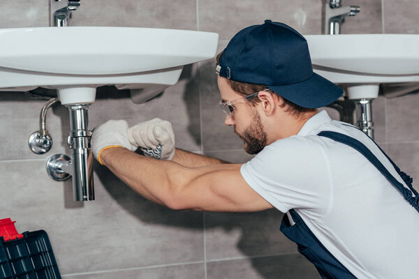 крупным планом молодой профессиональный сантехник чинит раковину в ванной комнате
