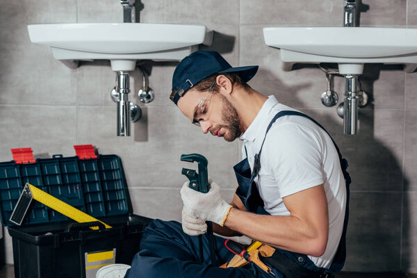 young professional plumber fixing sink in bathroom