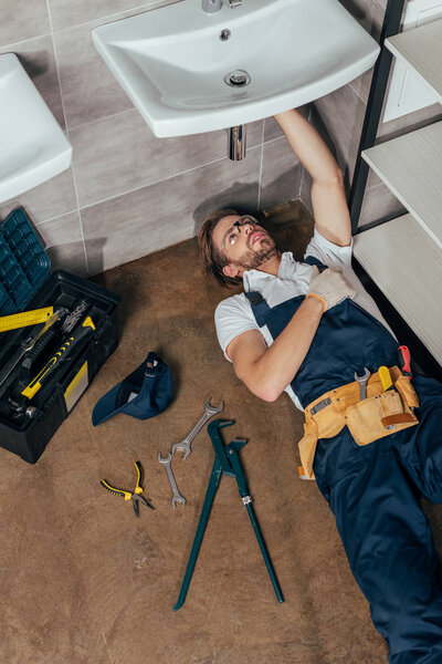high angle view of young male plumber fixing sink in bathroom