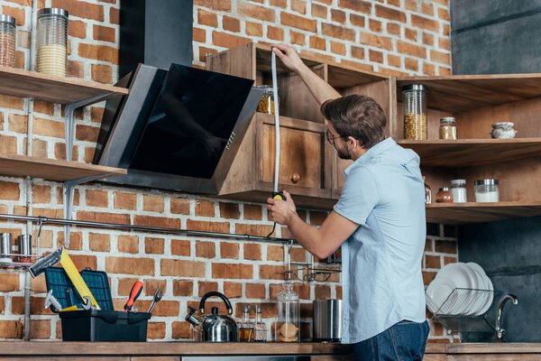 young man in eyeglasses measuring kitchen hood with tape