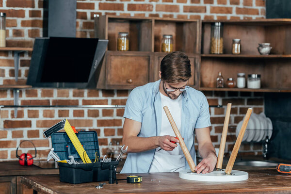 focused young man in eyeglasses holding screwdriver and repairing stool with screwdriver 
