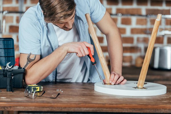 cropped shot of handsome young man repairing stool with screwdriver 