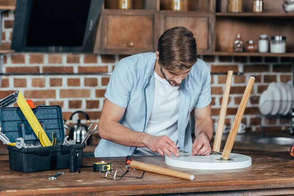 casual young man repairing stool with tools at home