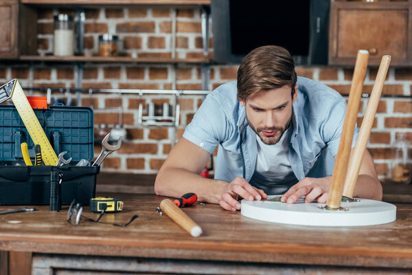 concentrated young man repairing stool with tools at home
