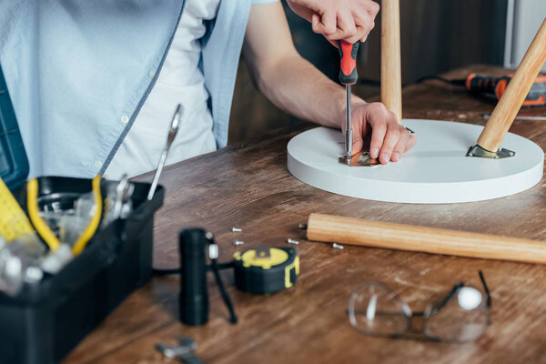 cropped shot of man repairing stool with screwdriver 