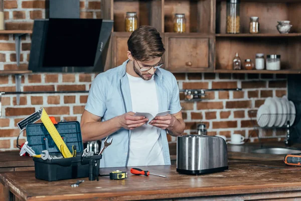 Young Man Eyeglasses Reading Manual While Repairinng Toaster Home — Stock Photo, Image