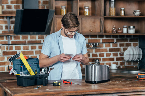young man in eyeglasses reading manual while repairinng toaster at home
