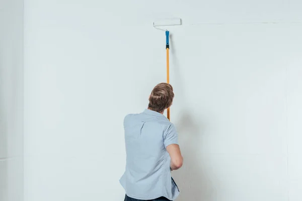 在家里粉刷墙壁时使用油漆滚筒的年轻人的背部视图 — 图库照片