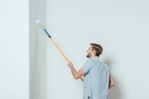 笑顔の若い男を自宅塗装壁中ペイント ローラーを使用しての側面図 — ストック写真