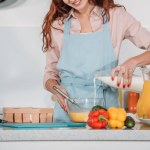 Cropped image of woman pouring milk in bowl to prepare batter