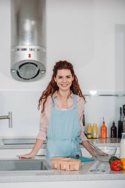 Mutfakta ayakta ve kameraya bakarak gülümseyen kadın