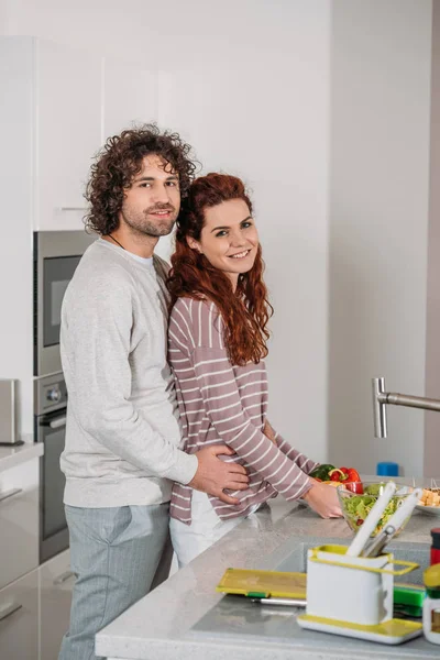 Boyfriend Hugging Girlfriend Back Kitchen Looking Camera — Free Stock Photo