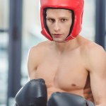 Joven boxeador muscular sin camisa mirando a la cámara en el gimnasio