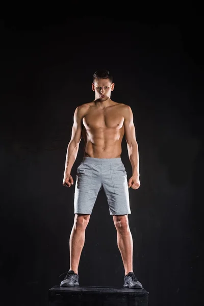 上半身裸の筋肉質スポーツマン ブロックの上に立って 黒のカメラ目線の完全な長さのビュー — ストック写真