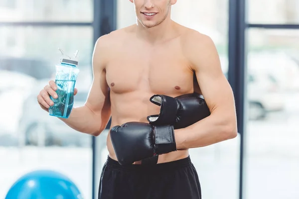 ボクシング グローブはジムでボトルから水を飲んで若い筋肉スポーツマンのショットをトリミング  — 無料ストックフォト