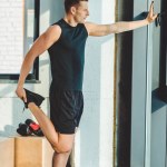 Side view of young man stretching before workout in gym