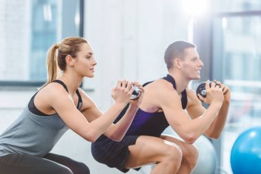 sporty young couple holding dumbbells and doing squat exercise in fitness studio clipart