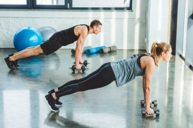 genç adam ve kadın spor salonunda dumbbells ile egzersiz yan görünüm