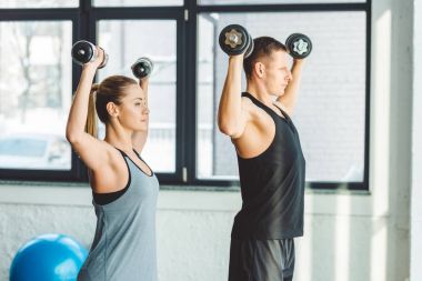 genç adam ve kadın spor salonunda dumbbells ile egzersiz yan görünüm