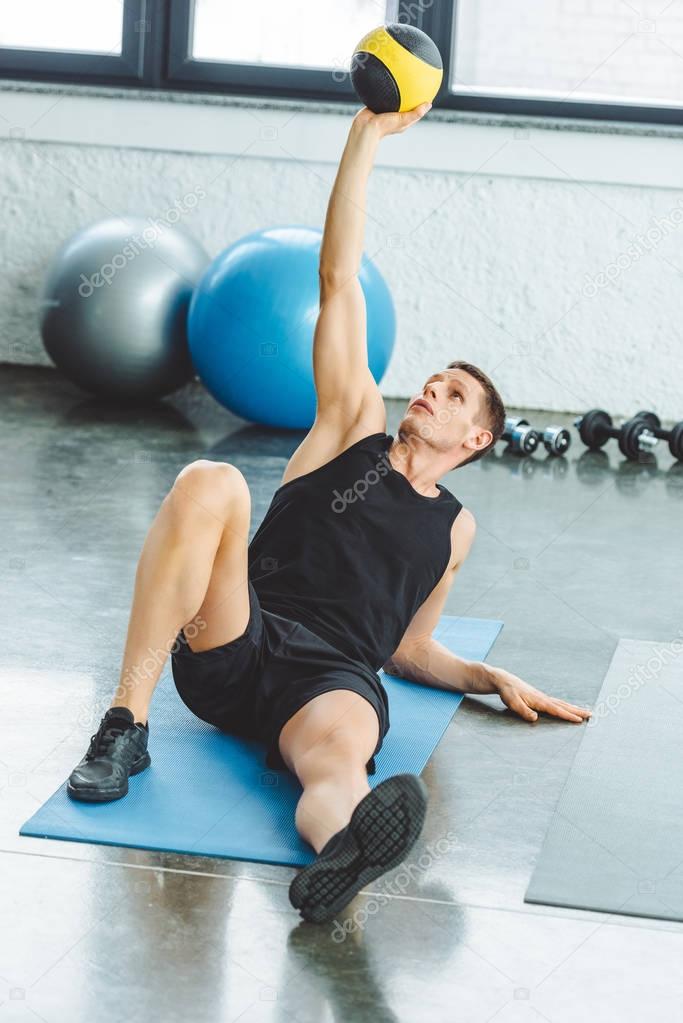 focused young sportsman exercising with ball in gym