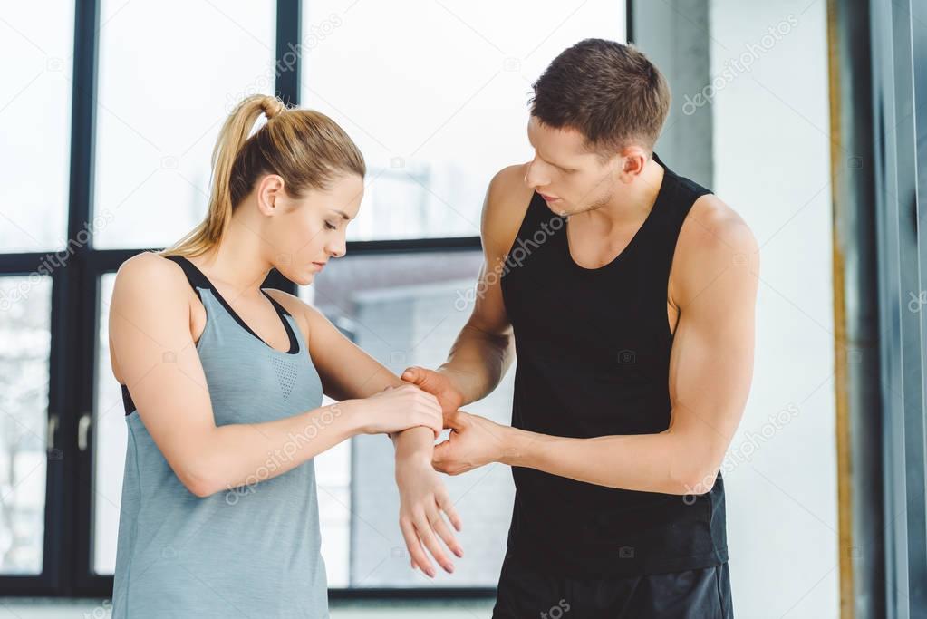 portrait of trainer holding injured arm of woman in gym