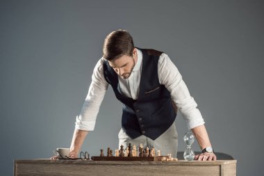 focused bearded stylish man looking at chess board with figures clipart