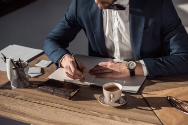 cropped shot of businessman writing in diary while sitting at table  clipart