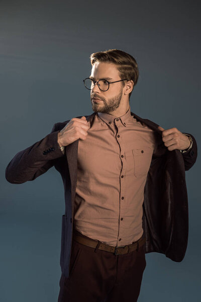portrait of stylish man in eyeglasses wearing jacket and looking away isolated on grey