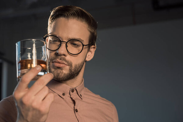 close-up view of stylish young man in spectacles holding glass of whisky 