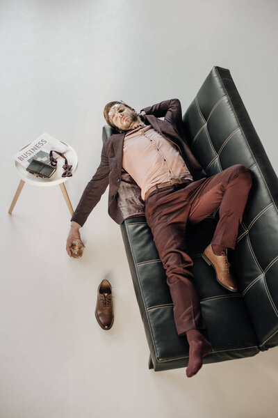 высокий угол зрения молодого бизнесмена без одной обуви, спящего на диване
