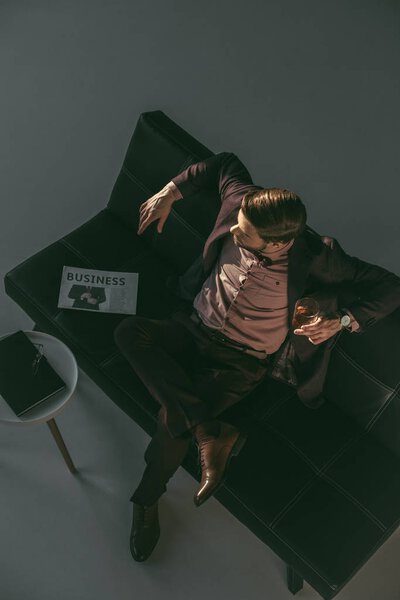 высокий угол зрения молодого человека, пьющего виски и отводящего взгляд, сидя на диване
