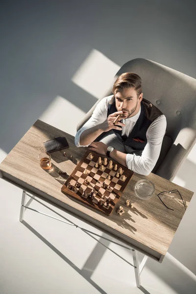 Focused man sipping alcoholic beverage while thinking about next chess move.  Stock Photo by DC_Studio