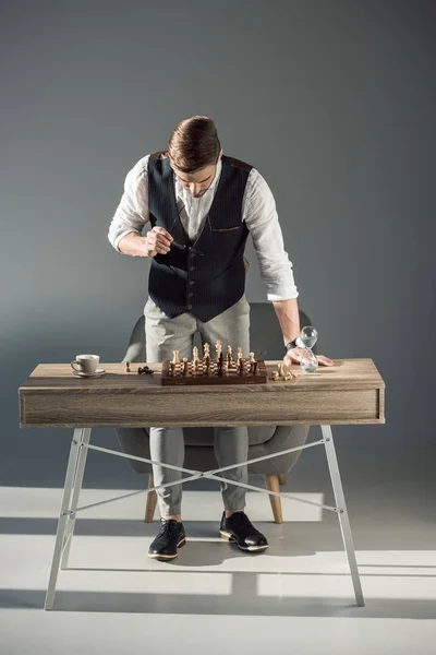 Stylish Young Man Holding Eyeglasses Looking Chess Board Figures — Free Stock Photo