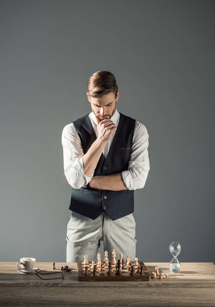 thoughtful young man looking at chess board with figures and sand clock