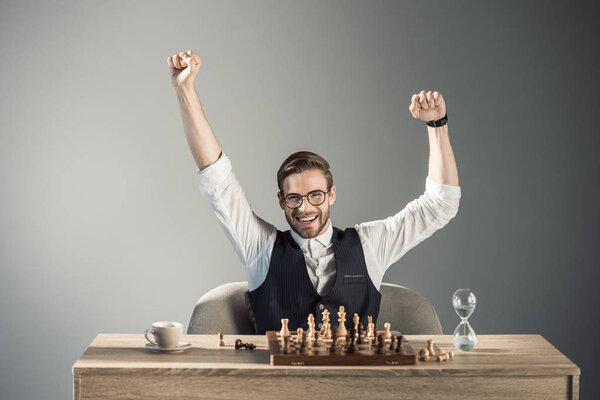 triumphing young busnessman in eyeglasses smiling at camera while playing chess 