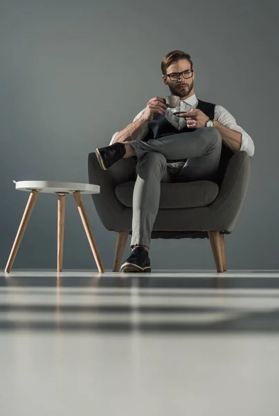 肘掛け椅子に座ってコーヒーのカップでスタイリッシュなビジネスマンのローアングル ビュー — ストック写真