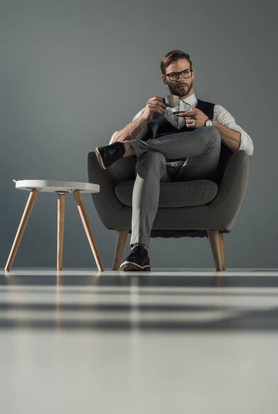 низкий угол зрения стильный бизнесмен с чашкой кофе сидя в кресле
