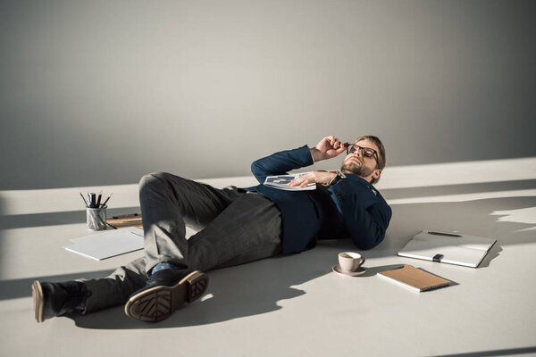 полный обзор молодого бизнесмена в очках, держащего газету и лежащего на полу
