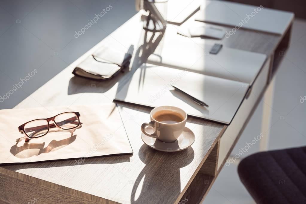 selective focus of eyeglasses on clipboard, cup of coffee and office supplies at workplace 