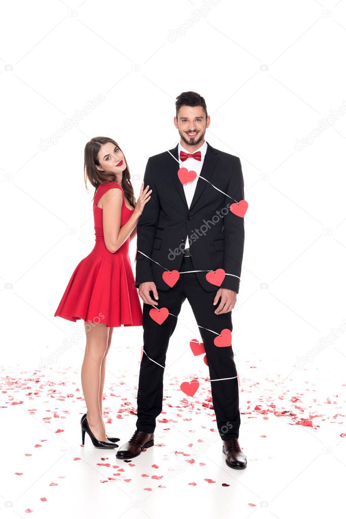 girlfriend standing near boyfriend bound with garland of hearts isolated on white, valentines day concept