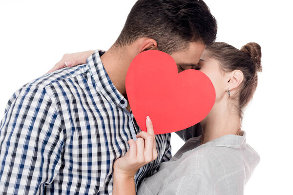 couple kissing and covering faces with paper heart isolated on white, valentines day concept