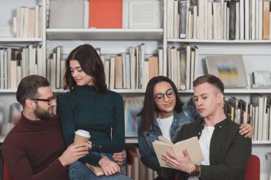 Kütüphane kitap ve kahve koltuklarda oturan mutlu çok kültürlü çiftler