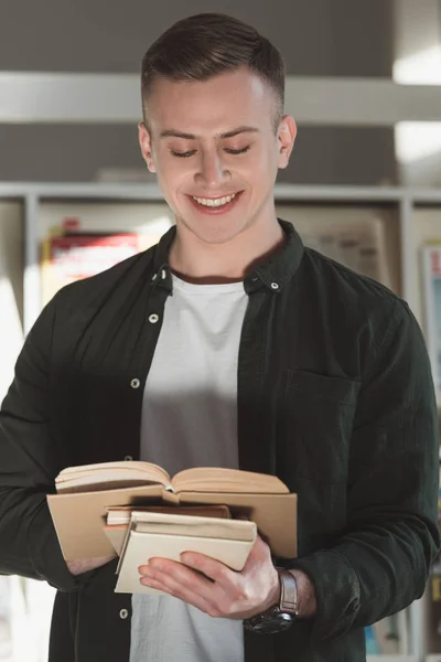 Χαμογελώντας Όμορφος Μαθητής Στέκεται Και Διαβάζοντας Βιβλίο Στη Βιβλιοθήκη — Φωτογραφία Αρχείου